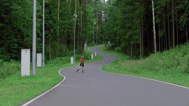 TRACKING Caucasian male professional biathlete roller skiing uphill on a forest track during mid-season practice in summer. ARRI Alexa Mini with Cooke S4 prime lenses RAW graded footage