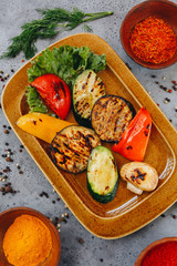 hot delicious grilled vegetables on a brown ceramic plate on a grey background