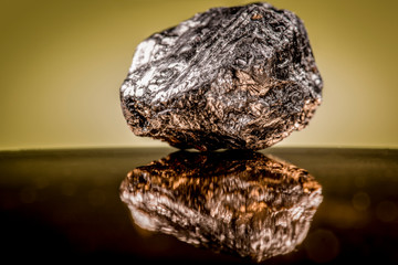 Small piece of heavy mineral rock with a dark exterior and gold features shining through against an...