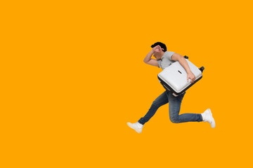 Fototapeta na wymiar Excited young Asian man tourist holding luggage and jumping isolated on orange background