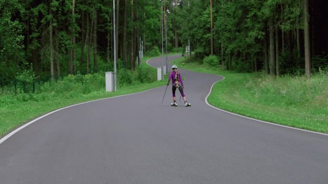 TRACKING Caucasian female professional biathlete roller skiing uphill on a forest track during mid-season practice in summer. ARRI Alexa Mini with Cooke S4 prime lenses RAW graded footage