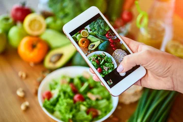 Papier Peint photo autocollant Manger Woman hands take smartphone food photo of vegetables salad with tomatoes and fruits. Phone photography for social media or blogging. Vegan lunch, vegetarian dinner, healthy diet