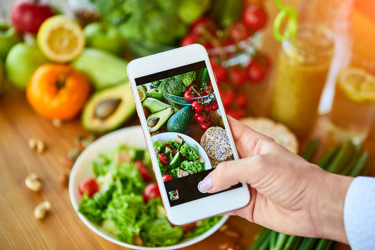 Woman hands take smartphone food photo of vegetables salad with tomatoes and fruits. Phone photography for social media or blogging. Vegan lunch, vegetarian dinner, healthy diet