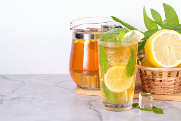 Glass of iced tea with mint and lemon on marble table. Cold drink.