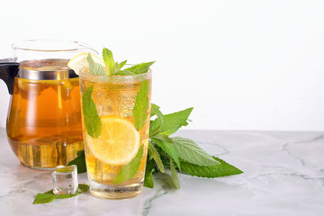 Glass of iced tea with mint and lemon on marble table. Cold drink.