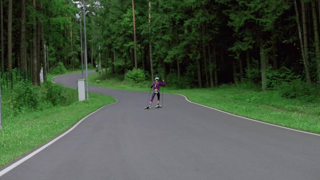 TRACKING Caucasian female professional biathlete roller skiing uphill on a forest track during mid-season practice in summer. ARRI Alexa Mini with Cooke S4 prime lenses RAW graded footage