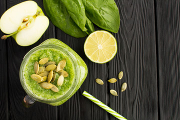 Green smoothies with spinach, apple and pumpkin seeds  on the black wooden background.Top view. Copy space.