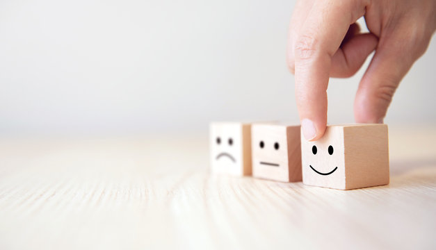 Close up customer hand choose smiley face and blurred sad face icon on wood cube, Service rating, satisfaction concept.