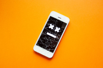 Broken smartphone with cracked destroyed screen on orange background with sad smile. Broken phone service, recovery and repair concept, symbol above.