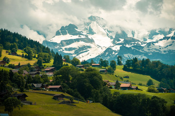 Obraz premium Amazing view of the hillside village and snowy slopes of the Swiss Alps. Colorful summer view of village. Idyllic outdoor scene in Switzerland, Europe