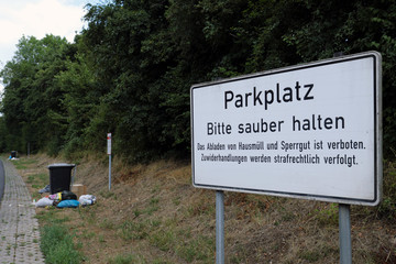 Volle Mülltonnen und Müll-Vandalismus auf Parkplatz an Bundesstraße mit Warntafel Parkplatz bitte sauber halten - Stockfoto