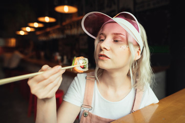 Closeup portrait of a cute girl eating sushi rolls with chopsticks at a Japanese restaurant.Concentrated looks at suschi roll in hand. Pretty lady posing with sushi roll on chopsticks. Asian cuisine