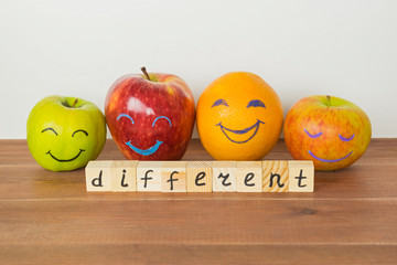 Different apples and orange with funny faces, tolerance, originality or friendship concept.