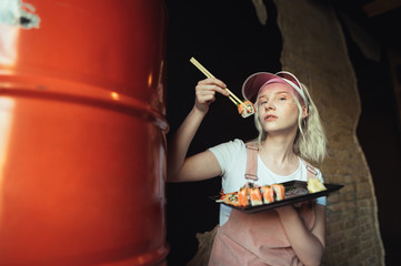 Stylish portrait of attractive girl with sushi rolloom in hand, holds on chopsticks, poses at...