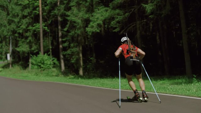 TRACKING Caucasian male professional biathlete roller skiing uphill on a forest track during mid-season practice in summer. ARRI Alexa Mini with Cooke S4 prime lenses RAW graded footage