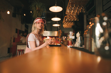 Beautiful woman in bright pink clothes sits in a restaurant at the bar, eats sushi rolls, drinks wine, looks into the camera with a serious face. Portrait of girl eating Japanese food at sushi bar