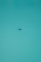 Vertical photography of a lone boat sailing at turquoise Oeschinensee in Switzerland. Swiss Oeschinen Lake. Aerial view, blurred boat. Minimalist nature. Escape, lost. Concept, abstract