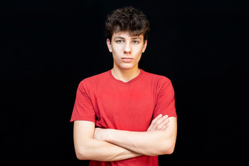 Portrait of a handsome teenage boy in a red T-shirt on a dark background. The guy has dark curly...
