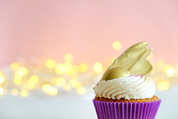Sweet organic cupcake in purple wrap with cream cheese frosting swirl and golden chocolate decoration on white wooden textured table. Close up, copy space, background.