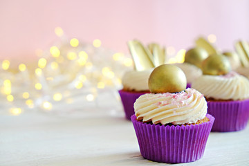 Sweet organic cupcake in purple wrap with cream cheese frosting swirl and golden chocolate decoration on white wooden textured table. Close up, copy space, background.