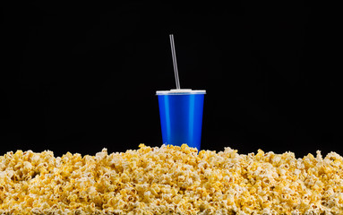 Blue cup with tube installed on scattered popcorn isolated on black background