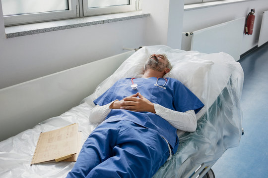 Exhausted doctor resting, sleeping on stretcher in hospital corridor