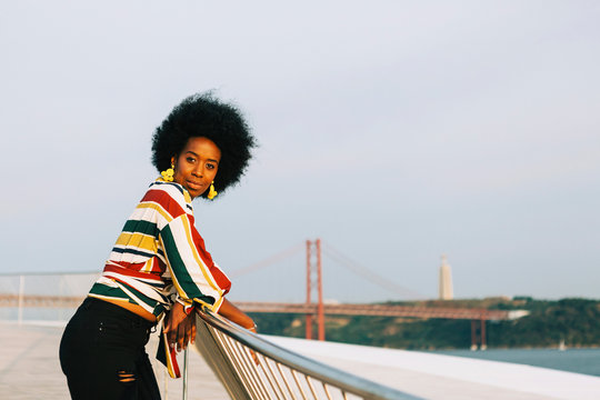 Portrait confident young woman at waterfront with 25 de Abril Bridge in background, Lisbon, Portugal