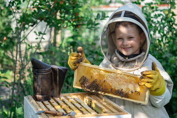 Cheerful boy beekeeper in protective suit near beehive. Honeycomb with honey. Organic food concept. The most useful organic honey.