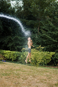 Water spraying boy in swim trunks in backyard