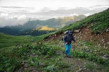 Man walking on the dirt road with hiking backpack and sticks on the hill