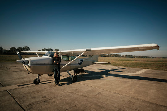 Male pilot standing at small propellor airplane on sunny tarmac