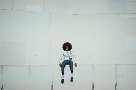 Portrait happy young man with afro sitting on wall