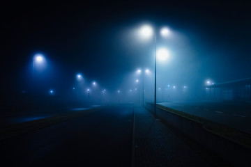 Street lamps illuminated over foggy, vacant road