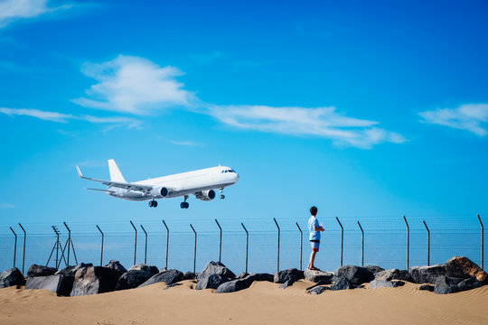 Boy on beach watching airplane flying low in blue sky near Lanzarote Airport, Spain