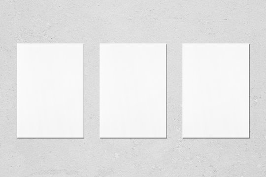 Three Empty White Vertical Rectangle Poster Mockups With Soft Shadows On Neutral Light Grey Concrete Wall Background. Flat Lay, Top View