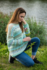 Obraz premium The girl in a knitted sweater poses with a flower on the lake