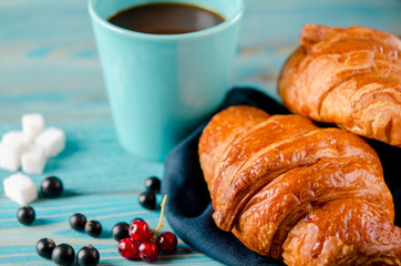 Fresh ruddy croissants with berries lie on a wooden table next to fresh black currant berries, red currants