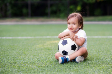 Portrait of sad unhappy boy sitting on football field and holding with both hands or embracing soccer ball. May be his team lost or he wanted to play but was rejected. Competition emotions concept