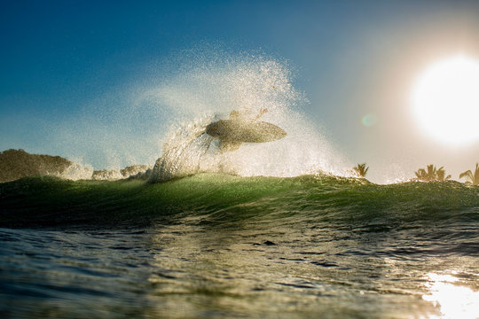 Surfer catching air behind ocean wave at sunrise, Sayulita, Nayarit, Mexico