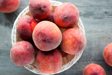 Ripe organic peaches in a white basket on a gray background.