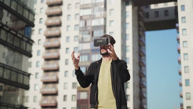 Tracking slow motion shot of young man in vr glasses standing outdoors in city street and exploring virtual reality