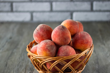 Ripe organic peaches in a brown basket on a gray background.