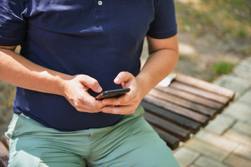 Man using smartphone on the bench in the park. Freelancer or blogger