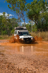 Fototapeta premium Western Australia – Flooded Outback gravel road with 4WD car crossing the waterhole with splashing muddy water at the savanna