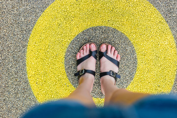 Black slippers standing in yellow circle on the asphalt concrete floor. Concept of limit, boundary, frame, etc.