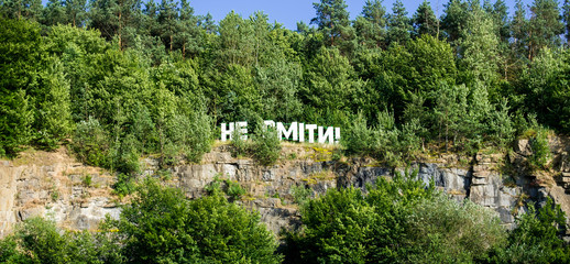 Fototapeta na wymiar Rock overgrown with dense forest. The inscription on the rock reads 
