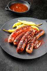 Traditional barbecue German Bratwurst with hot sauce and peperoni as closeup on a modern design cast iron plate
