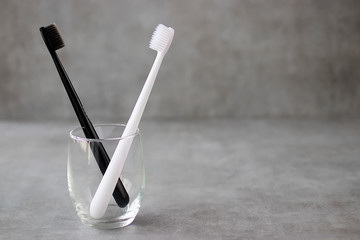Black and white toothbrushes in a glass beaker on a gray background.