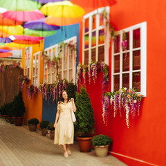 Fototapeta premium Travel tourist brunette woman in yellow dress walks the streets with bright decoration of the city. Tilt-shift lens blur