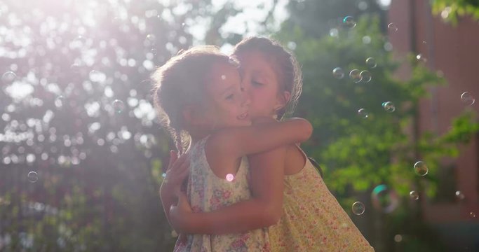 Authentic shot of two cute little girls sisters hugging having fun playing with soap bubbles outside their house on a sunny day.